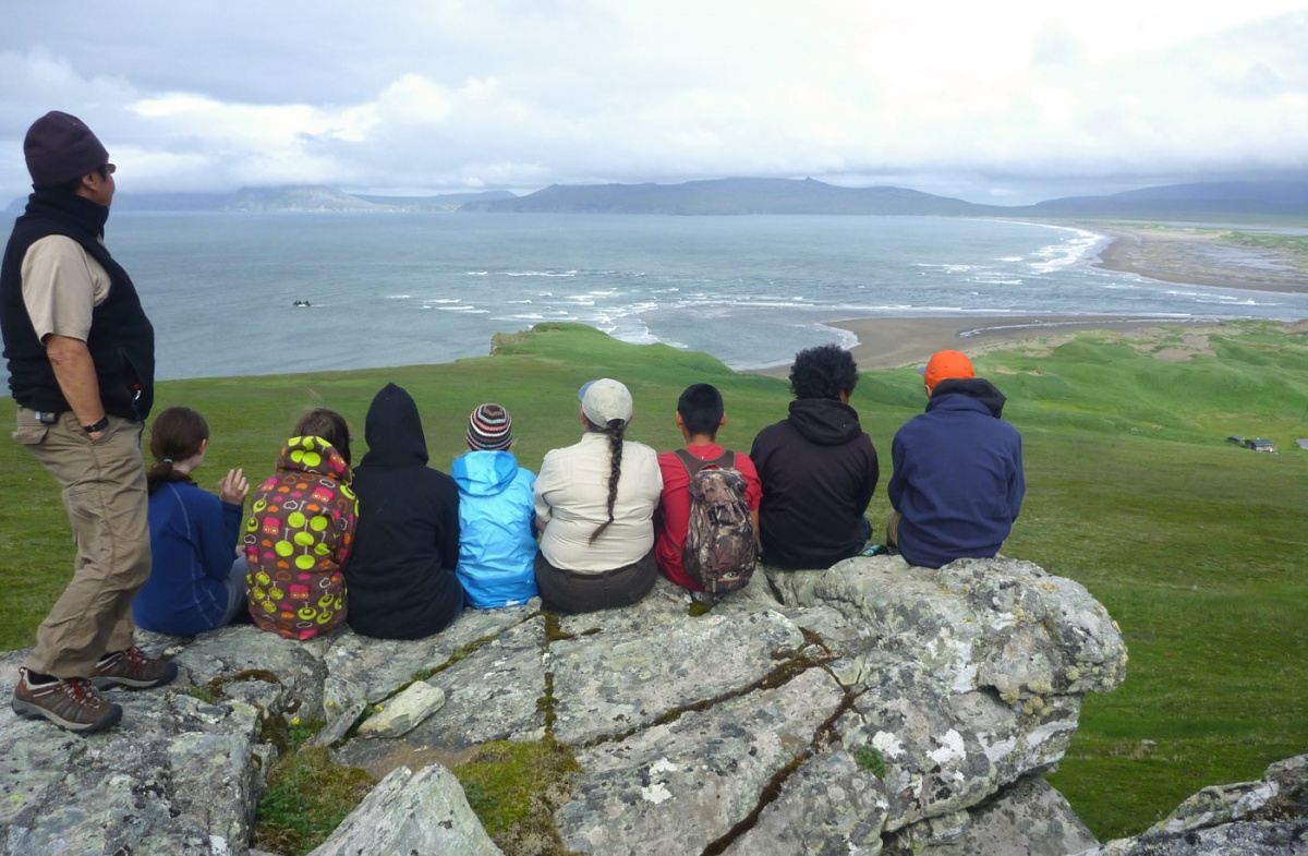 A group of young people sitting on a rock and looking out over a large body of water in Alaska.