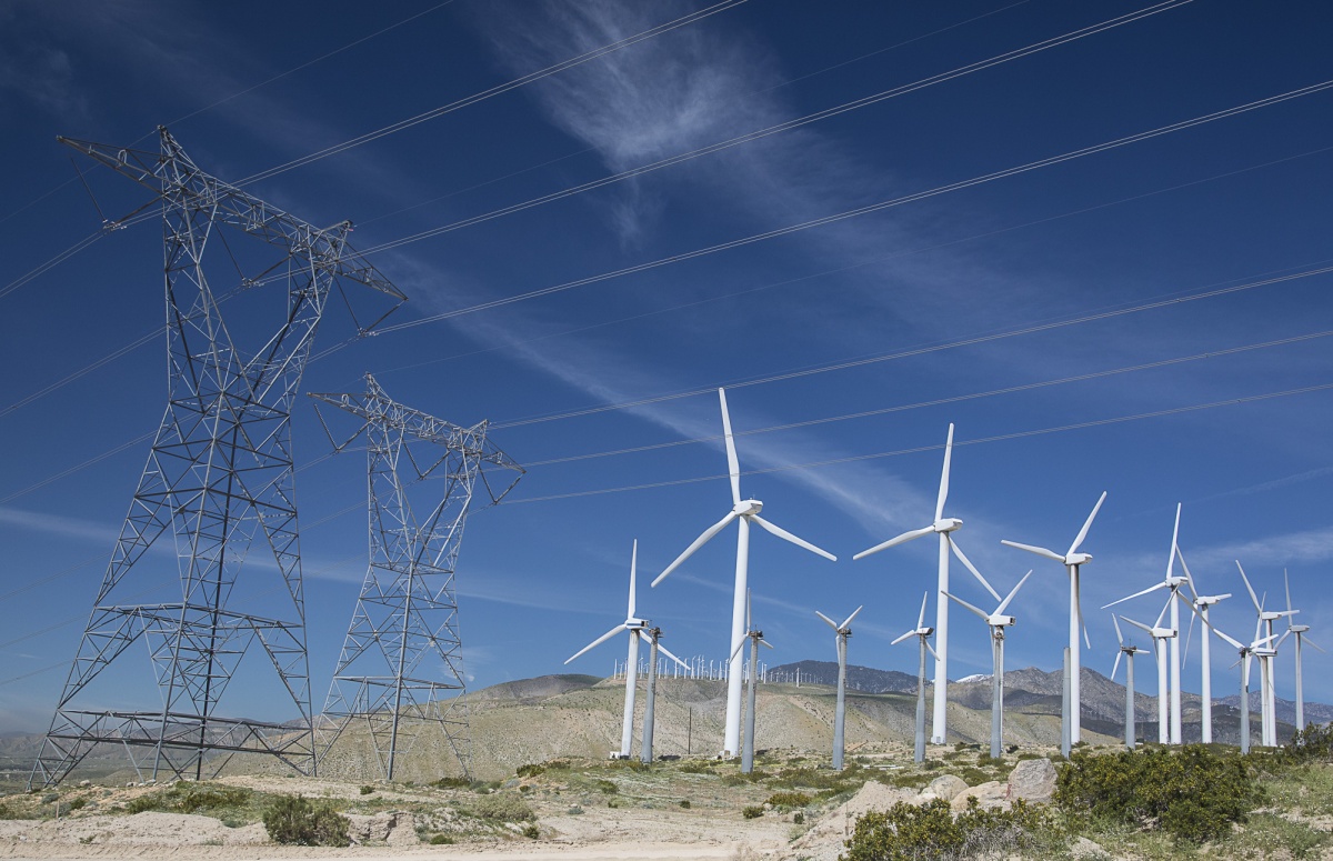 Power lines and wind turbines tower into the sky on a rocky plain. 